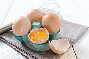 Fresh raw chicken eggs in an cartons egg box. Broken egg, yolk. Organic food for good health high protein on white wooden