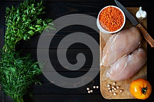 Fresh raw chicken fillet on a cutting board with herbs and vegetables on a dark background. Diet food top view with place for text