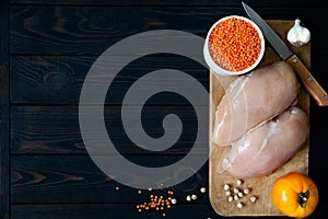 Fresh raw chicken fillet on a cutting board with vegetables on a dark background. Diet food top view with place for text