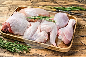 Fresh raw chicken meat, wings, breast, thigh and drumsticks on a wooden tray. Wooden background. Top view