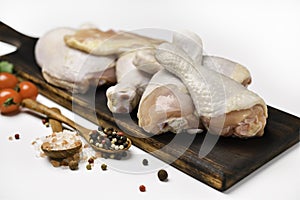 Fresh raw chicken thighs with ingredients for cooking on a wooden cutting board on white background