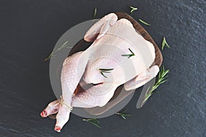 Fresh raw chicken whole on black plate background / rosemary chicken meat wooden cutting board