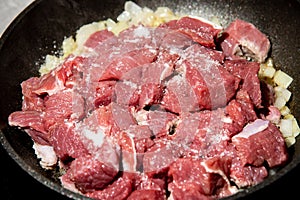 Fresh raw chopped meat and onion with salt in a frying pan