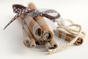 Fresh raw cinnamon sticks on white background tied with brown dotted bow and jute rope
