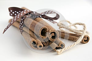 Fresh raw cinnamon sticks on white background tied with brown dotted bow and jute rope