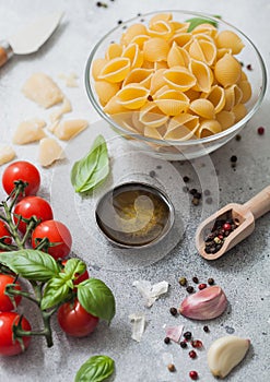 Fresh raw classic conchiglie  pasta in glass bowl with parmesan cheese and tomatoes, oil and garlic with basil on light background