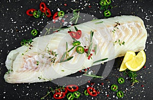 Fresh Raw Cod loin fillet with rosemary, chillies, cracked pepper and lemon on stone board