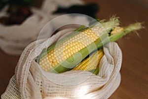 Fresh raw corn in eco canvas grocery bag. Cotton bags on wooden table. Zero waste shopping concept. Plastic free items