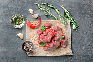 Fresh raw cut meat with spices, herbs and oil on grey textured background