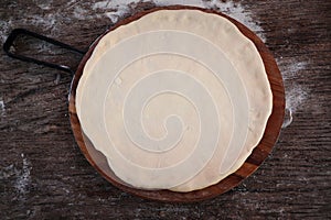 Fresh raw dough for pizza or bread baking on wooden cutting board on dark rustic background. Top view