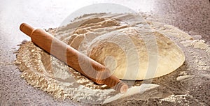Fresh raw dough and rolling. Raw dough for pizza or bread baking. Rolled doughs with rolling pin on table covered baking