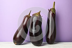 Fresh raw eggplants on white wooden table against violet background