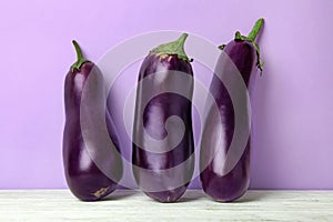 Fresh raw eggplants on white wooden table against violet background