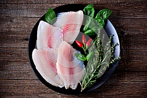 Fresh raw fillet of tilapia fish with thyme, rosemary, basil and chili pepper.