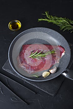 Fresh raw flank steak beef in the pan with rosemary, garlic, olive oil on dark background. Classic marinades recipe for