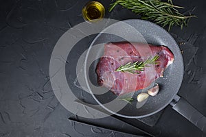 Fresh raw flank steak beef in the pan with rosemary, garlic, olive oil on dark background. Classic marinades recipe for