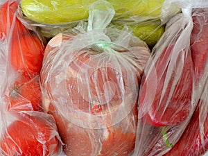 Fresh raw foods in plastic bags just bought by weight: a piece of pork meat, two zucchini, few red tomatoes and red peppers