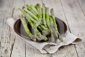 Fresh raw garden asparagus closeup on brown ceramic plate and linen napkin on rustic wooden table background. Green spring