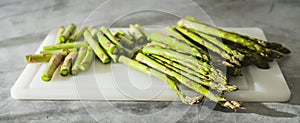 Fresh raw green asparagus close-up on a white cutting board on a grey background