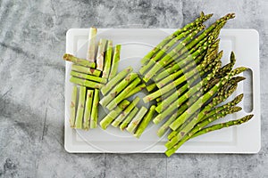 Fresh raw green asparagus on a white cutting board close-up on the kitchen table, flat lay, copy space