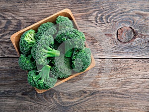 Fresh raw green broccoli in wooden bowl on wooden background, to