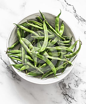 Fresh raw green string beans in a white bowl on a light marble background