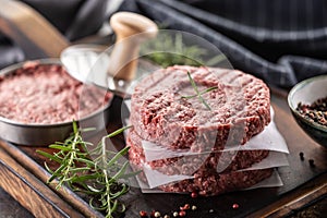 Fresh raw ground beef patties with rosemary salt and pepper made in a meat form on a cutting board