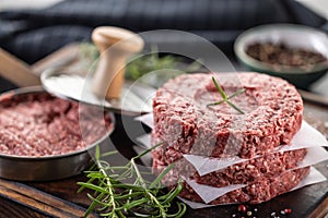 Fresh raw ground beef patties with rosemary salt and pepper made in a meat form on a cutting board