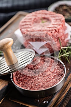 Fresh raw ground beef patties with rosemary salt and pepper made in a meat form on a cutting board