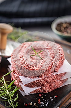 Fresh raw ground beef patties with rosemary salt and pepper made in a meat form on a cutting board