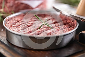 Fresh raw ground beef patties with rosemary salt and pepper made in a meat form on a cutting board