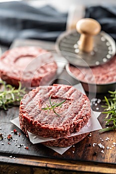 Fresh raw ground beef patties with rosemary salt and pepper made in a meat form on a cutting board