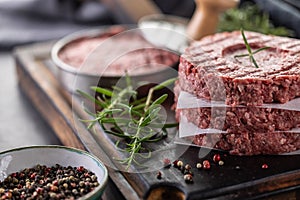 Fresh raw ground beef patties with rosemary salt and pepper made in a meat form on a cutting board