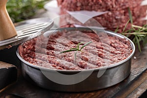 Fresh raw ground beef patties with rosemary salt and pepper made in a meat form on a cutting board