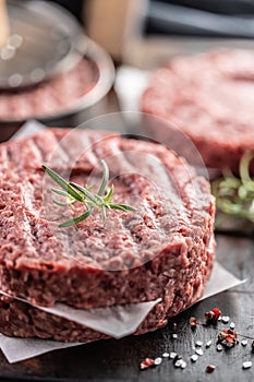 Fresh raw ground beef patties with rosemary salt and pepper made in a meat form on a cutting board