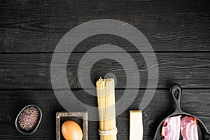 Fresh raw ingredients for traditional italian pasta Carbonara, on black wooden background, top view flat lay, with copy space for