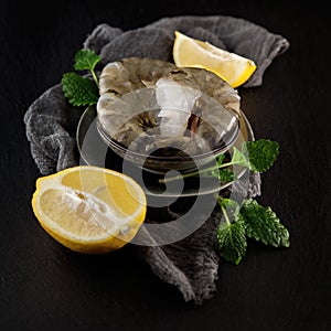 Fresh raw king prawns with lemon and lemon balm on dark slate kitchen plate