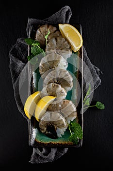 Fresh raw king prawns with lemon and lemon balm on dark slate kitchen plate