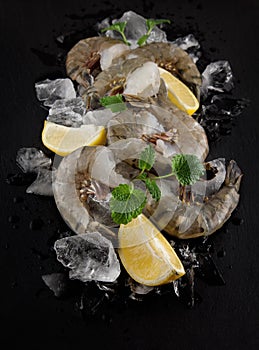 Fresh raw king prawns with lemon and lemon balm on dark slate kitchen plate