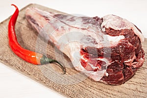 Fresh raw lamb bone on wooden cutting board with hot red pepper