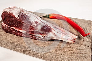 Fresh raw lamb bone on wooden cutting board with hot red pepper