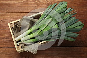 Fresh raw leeks in crate on wooden table, top view