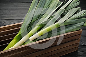 Fresh raw leeks in wooden crate on black table, closeup