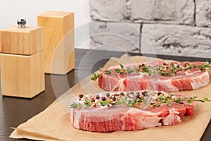 Fresh raw marbled meat steak with thyme and seasoning on brown parchment paper on a black table against a gray brick wall bac