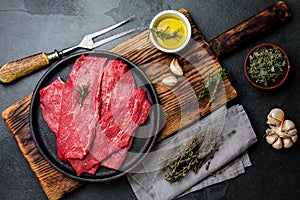 Fresh raw meat beef steaks. Beef tenderloin in cast iron pan on wooden board, spices, herbs, oil on slate gray background. Food ba