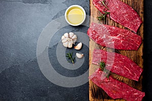 Fresh raw meat beef steaks. Beef tenderloin on wooden board, spices, herbs, oil on slate gray background. Food background with cop