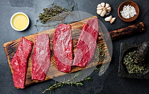 Fresh raw meat beef steaks. Beef tenderloin on wooden board, spices, herbs, oil on slate gray background. Food cooking