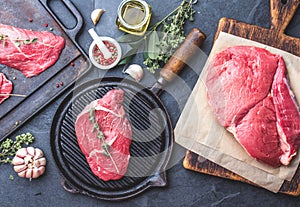 Fresh raw meat. Beef Tenderloin and marbled beef steaks on grill pan and frying board with seasoning, black background top view