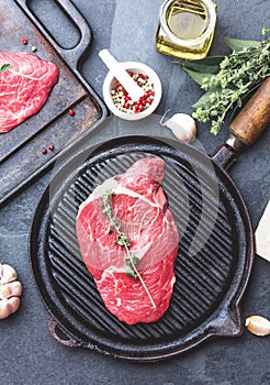 Fresh raw meat. Beef Tenderloin and marbled beef steaks on grill pan and frying board with seasoning, black background top view