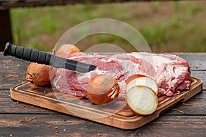 Fresh raw meat with onion and black knife on wooden plate